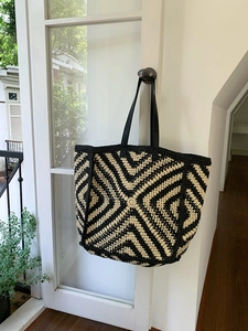 Detail of hand-woven striped tote bag featuring beige geometric patterns and black straps