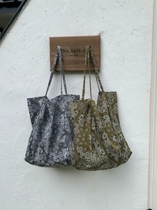 Detail of grey and olive green canvas tote bags featuring paisley patterns on wall hooks