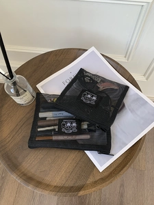 Detail of two black mesh organizer bags with bear patches on a wooden tabletop