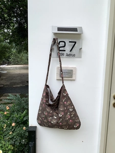 Outdoor shot of a casual floral canvas tote bag hanging on a white wall with 27 Hope Avenue sign