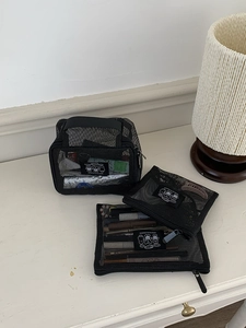 Three-piece black mesh toiletry bag set with cartoon labels on a minimalist white desk