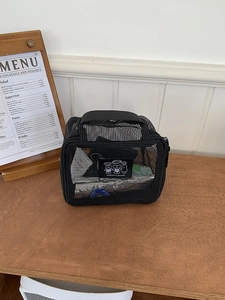 Detail of black mesh travel organizer bag with cartoon patch and top handle on wooden table