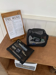 Detail view of black mesh travel pouches with zippers on a wooden shelf