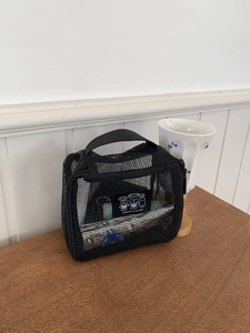 Detail of black mesh travel bag with handle on wooden surface showing semi-transparent nylon