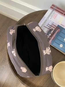 Top view of large gray bear print makeup bag with black lining on a wooden desk