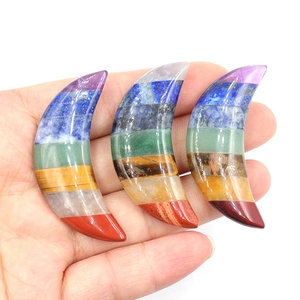 Three crescent moon stones with seven colorful chakra layers held in hand on white background
