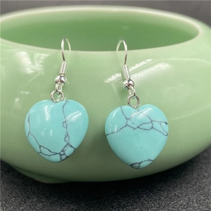 Detail of heart-shaped turquoise stone earrings hanging on a green ceramic bowl
