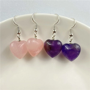 Detail of amethyst and rose quartz heart earrings with silver hooks on a ceramic tray