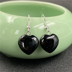 Polished black heart-shaped stone earrings on a green ceramic bowl for display