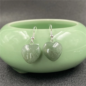 Detail of light green heart-shaped quartz earrings hanging on a green ceramic bowl