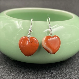 Macro shot of red heart-shaped natural stone earrings hanging on a green bowl edge