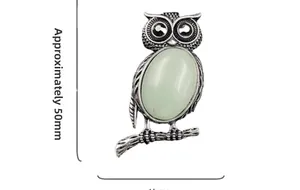 Macro detail of owl pendant brooch with green gemstone and intricate silver feather texture