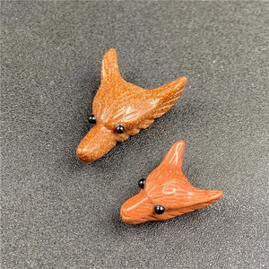 Macro shot of two fox head pendants carved from warm brown goldstone with sparkles