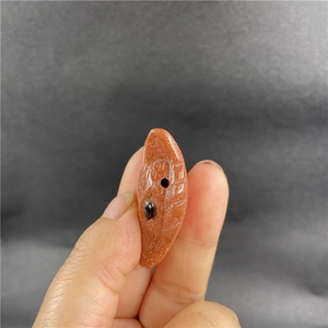 Close-up of leaf-shaped gold sandstone pendant with sparkling flecks held by hand