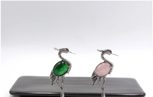 Detailed view of crane brooches featuring green agate and pink crystal shell gemstones