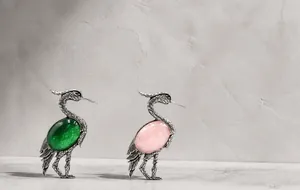 Detailed view of vintage crane brooches with emerald green and pink oval gemstones