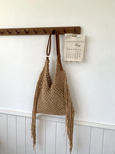 Bohemian woven tote bag with fringe tassels and brown leather strap on wooden hook