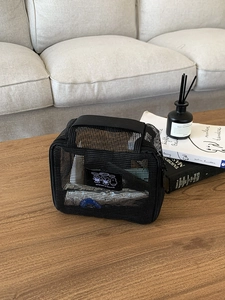 Detail view of black mesh travel toiletry bag with handle on a wooden coffee table