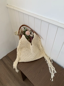 Close-up of beige hollow knit tote bag with long fringe tassels and brown leather handles