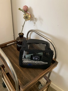 Detail of black mesh toiletry bag with woven handle and graphic patch on wooden cart