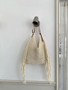 Detail of bohemian hollow knit tote bag featuring white tassels and brown leather strap