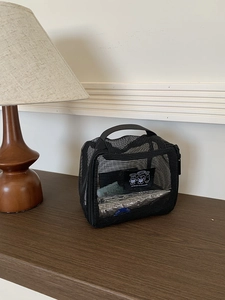 Close-up of black mesh toiletry bag with handle and cartoon patch on wooden surface