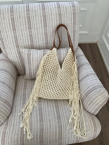 Detail of bohemian crochet tote bag featuring long tassels and brown leather handle straps