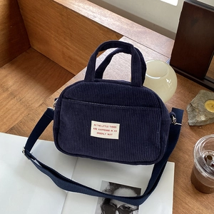 Dark blue corduroy crossbody bowling bag with adjustable strap on a wooden table