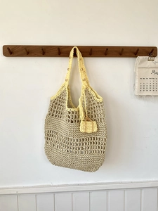Detail van de geweven rieten tas met rasterpatroon, gele franjes en houten kralen sieraad