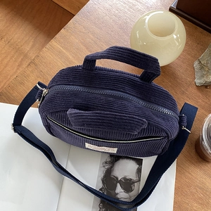Blue corduroy mini bowling bag with dual handles and woven strap on wooden table