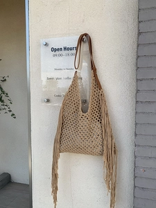 Detail of bohemian hand-woven tote bag featuring long fringes and brown leather handle