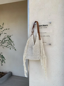Detail of bohemian knit tote bag with long fringe tassels and brown leather shoulder strap