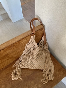 Close-up of beige woven tote bag featuring long side tassels and brown leather strap