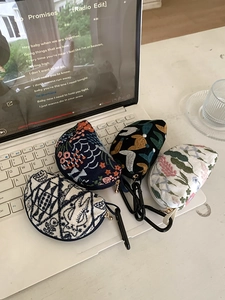 Detail of embroidered headphone cases with floral patterns and metal carabiners on a laptop