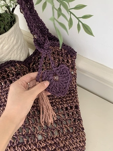 Detail van strooien tas met paarse hartvormige hanger, kraal en kwastje decoratie
