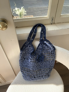 Detail van de donkerblauwe rieten tas met hol maaspatroon en een kwastje als sieraad