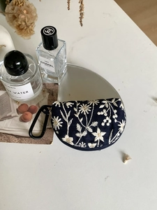 Close-up of dark blue embroidered daisy storage pouch with a convenient black carabiner