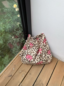Leopard print canvas tote bag with pink bow pattern on a wooden floor background