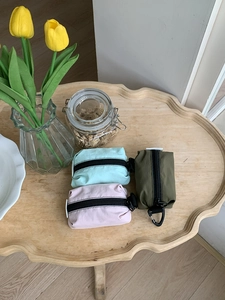 Trois mini pochettes en nylon colorées avec zips et anneaux en D sur une table en bois