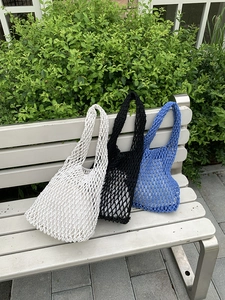 Detail view of handmade woven tote bags in white, black and blue on a garden bench