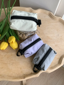 Trois mini pochettes en nylon beige, violet et gris sur un plateau en bois