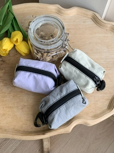 Trois mini pochettes en nylon violet, gris et crème avec mousquetons sur plateau bois