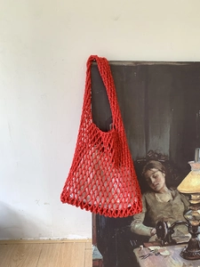 Detail of red hand-woven tote bag with white inner pouch hung against a vintage oil painting