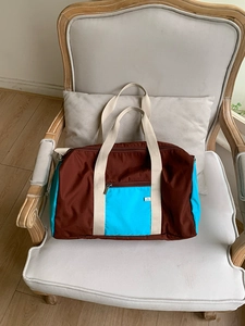 Detail of color-block nylon tote bag with brown and blue panels on a wooden chair