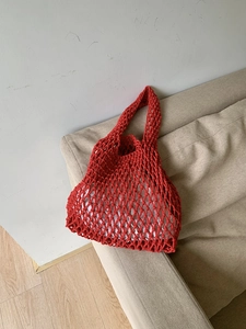 Detail of red hand-woven large mesh tote bag with wide shoulder strap on sofa