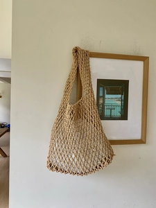Detail of hand-woven hollow mesh tote bag with white inner pouch on a wall hanger