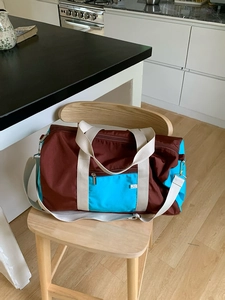 Detail of color-block nylon tote bag with reinforced handles and adjustable strap on a chair