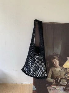 Artistic display of a hand-woven black mesh tote bag hanging on a classic portrait frame