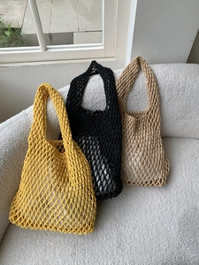 Close-up of three woven mesh tote bags in yellow black and beige on a white sofa