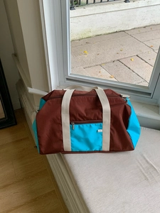 Close-up of color-block nylon tote bag showing front zipper pocket and metal buckle detail